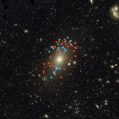 Diese tiefe Aufnahme zeigt den großen Halo um die große elliptische Galaxie Messier 87. Die roten und blauen Punkte in diesem Bild kennzeichnen die Positionen Planetarischer Nebel in der Galaxie Messier 87, deren Bewegungen verraten haben, das es vor nicht allzu langer Zeit zu einem Zusammenstoß mit einer kleineren Galxie gekommen sein muss, die nun vollständig mit Mesier 87 verschmolzen ist. Bezogen auf die Galaxie als solche bewegen sich die rot markierten Planetarischen Nebel von uns weg und die blau markierten auf uns zu.